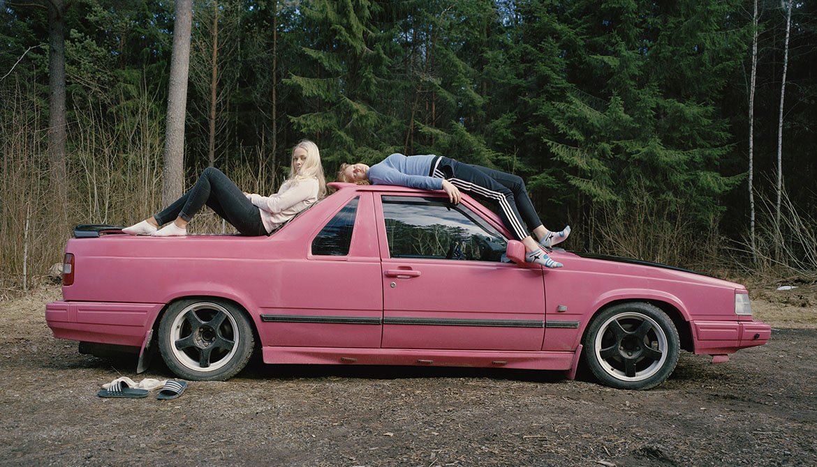 Två tjejer poserar sittand och liggande på sin rosamålade Volvo EPA. 
