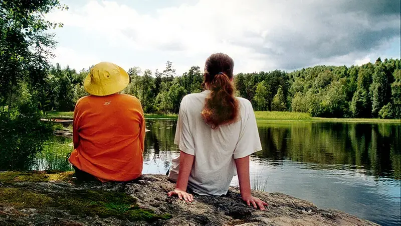 Två barn sitter på ett berg och tittar ut över vattnet.
