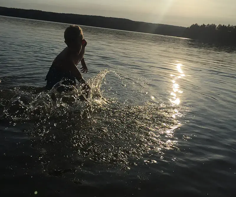 Pojke plaskar och badar i en sjö en härlig sommarkväll.