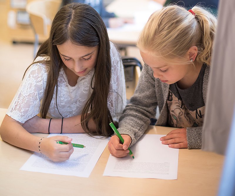Två tjejer sitter i skolbänken och arbetar tillsammans. 